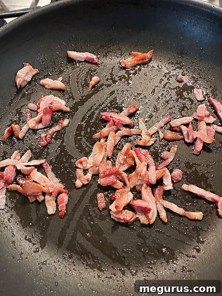 Crispy bacon sizzling in a skillet, rendering its fat to create a flavorful base.