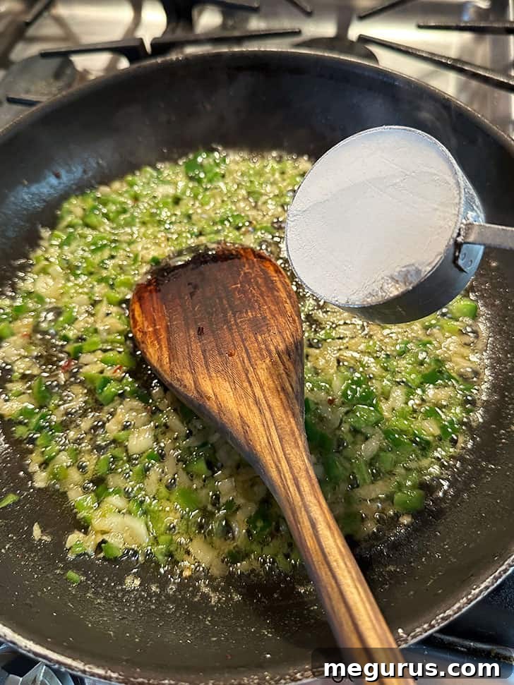 Finely diced jalapeños and onions being sautéed in butter and bacon fat, creating an aromatic base for the cheese sauce.