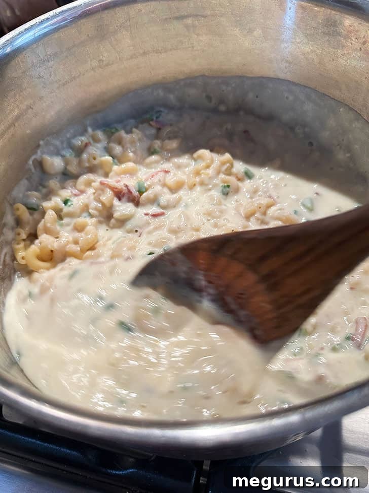 The luxurious cheese sauce being poured over perfectly cooked macaroni in a large pot, ready to be combined.