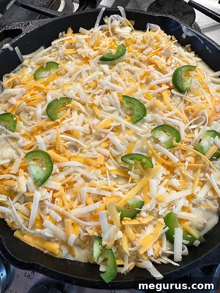 The combined macaroni and cheese layered in a cast iron skillet, topped with additional cheese and jalapeño slices, ready for baking.