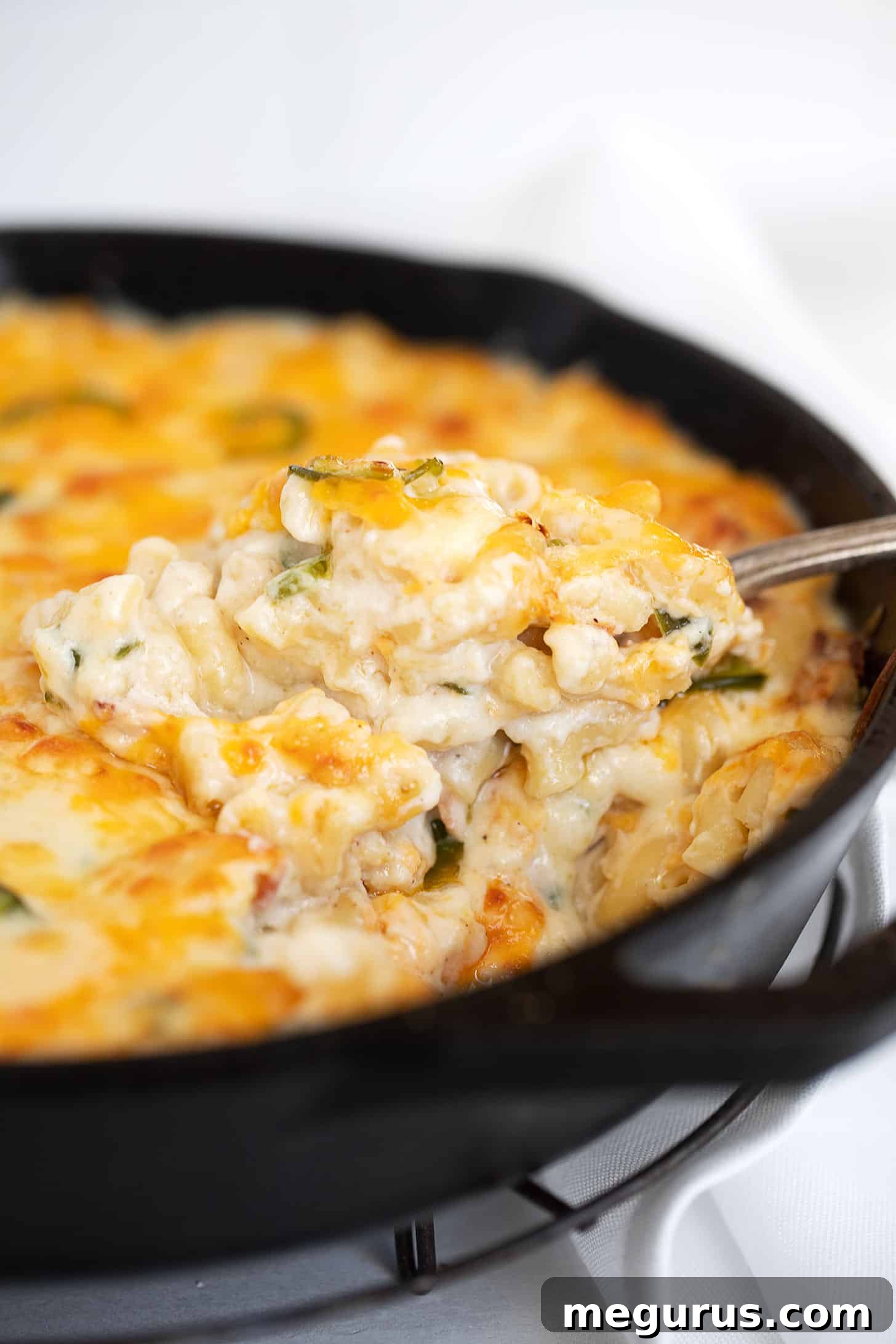 Close-up of baked jalapeño mac and cheese in a cast iron skillet, with a spoon taking out a creamy, cheesy portion.