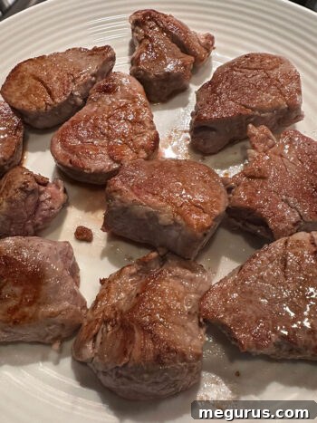 Perfectly browned pork medallions resting on a plate after searing.