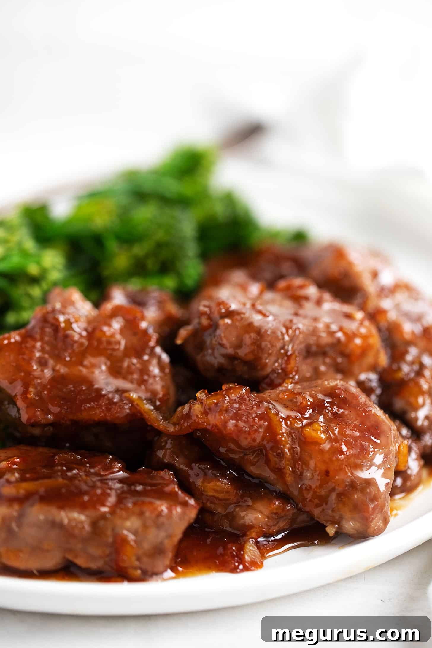 A close-up of a plate of orange pork medallions, glistening with sauce, accompanied by steamed broccolini.