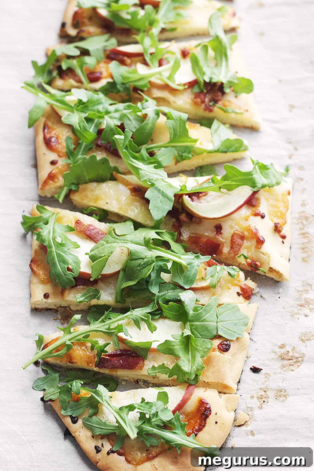 Close-up of baked cheddar, pancetta, and apple flatbread on parchment paper.