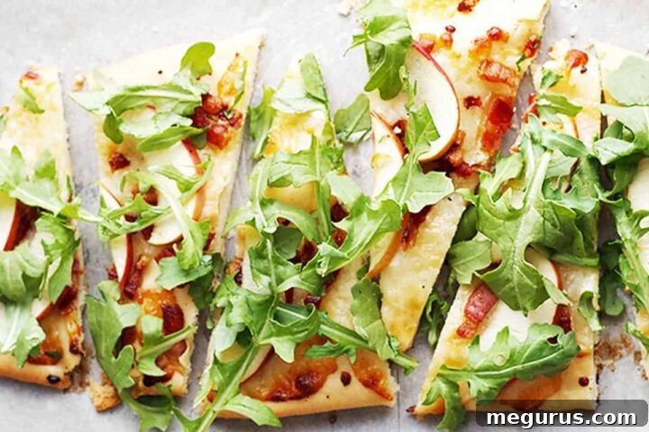 Close-up of a slice of cheddar, pancetta, and apple flatbread garnished with fresh arugula.