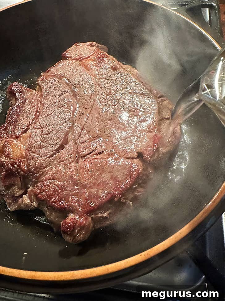 Adding water to the pan around the browned beef, forming the base of the braising liquid for slow cooking barbacoa.