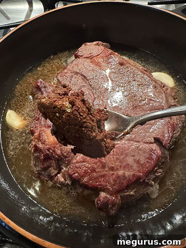 Incorporating a flavorful seasoning mixture, smashed garlic, and a bay leaf into the braising liquid with the beef, ready for slow cooking.