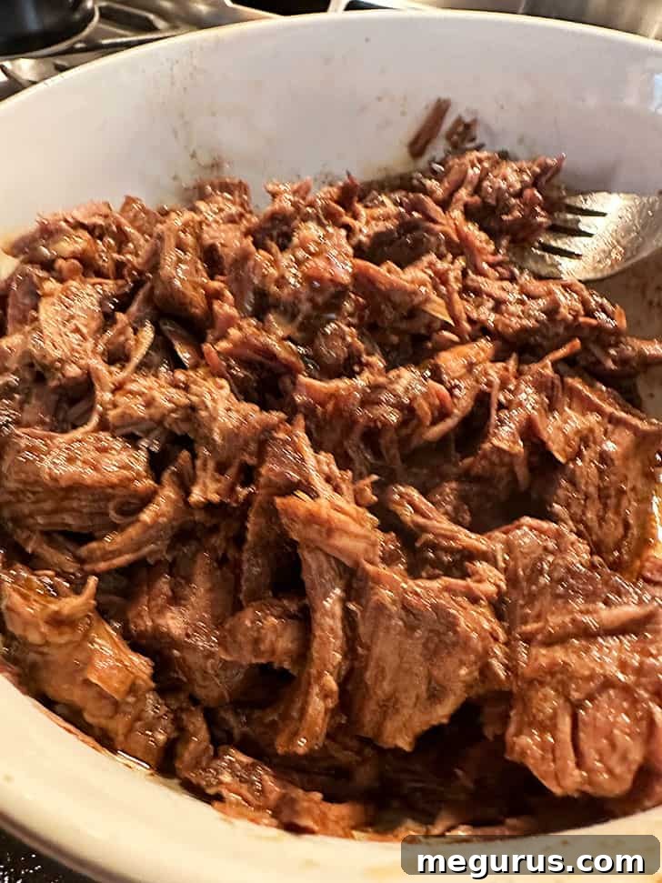 Shredded barbacoa beef generously coated and mixed with the strained, rich braising sauce, creating a deeply flavorful finished product.