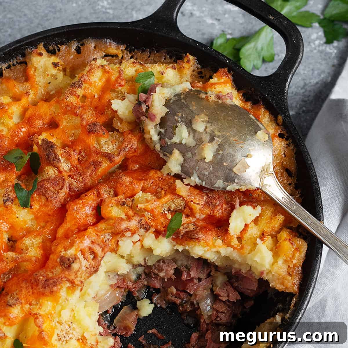 Hearty Corned Beef Cottage Pie in a rustic skillet, topped with golden mashed potatoes and melted cheese, with a serving spoon.