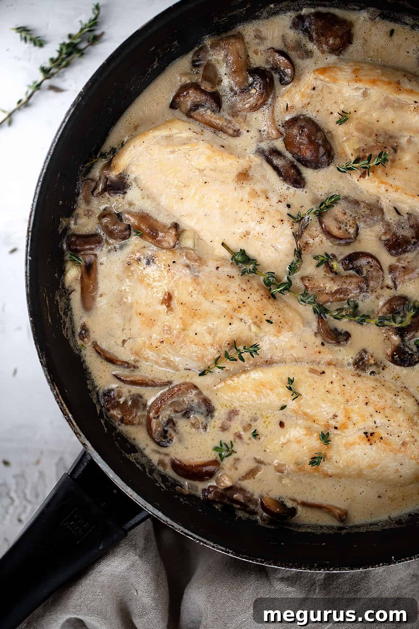 Close-up of creamy garlic chicken with mushrooms in skillet, garnished with fresh herbs.