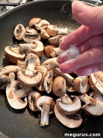 Mushrooms being sautéed in a skillet, seasoned with salt