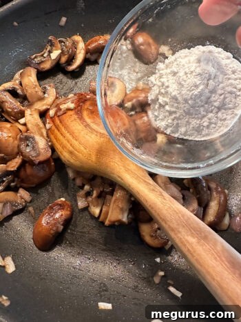 Flour being sprinkled over the cooked mushrooms, shallots, and garlic in the skillet