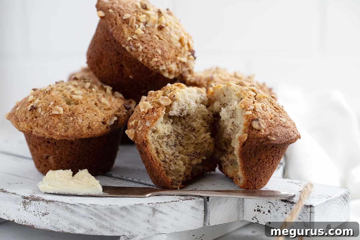 Golden-brown banana walnut muffins generously topped with chopped walnuts, arranged on an elegant white serving platter, ready to be enjoyed.