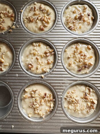 Muffin cups filled with batter and topped with chopped walnuts, ready for baking.