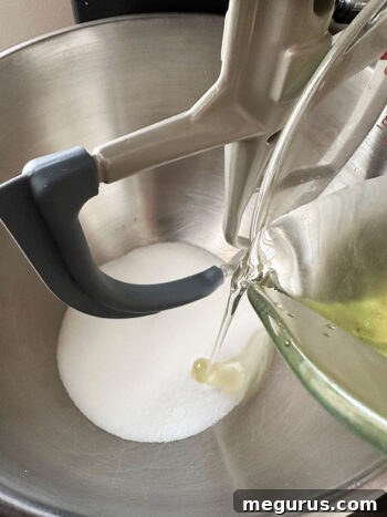 Granulated sugar and vegetable oil being mixed together in a large mixing bowl.