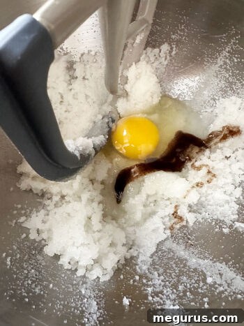 An egg and vanilla extract being added to the creamed sugar and oil mixture.