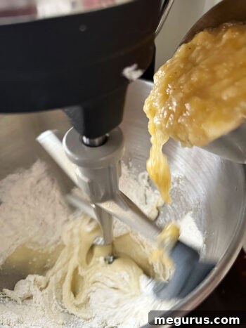Mashed bananas being folded into the muffin batter for even distribution.