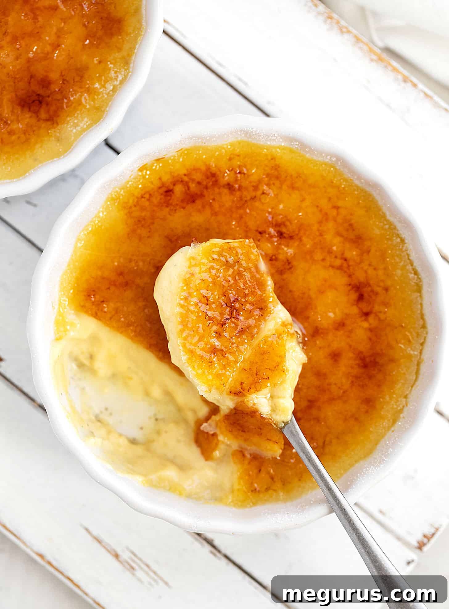 A close-up of a maple crème brûlée in a ramekin, showing the perfect caramelized sugar top and a spoon breaking through it