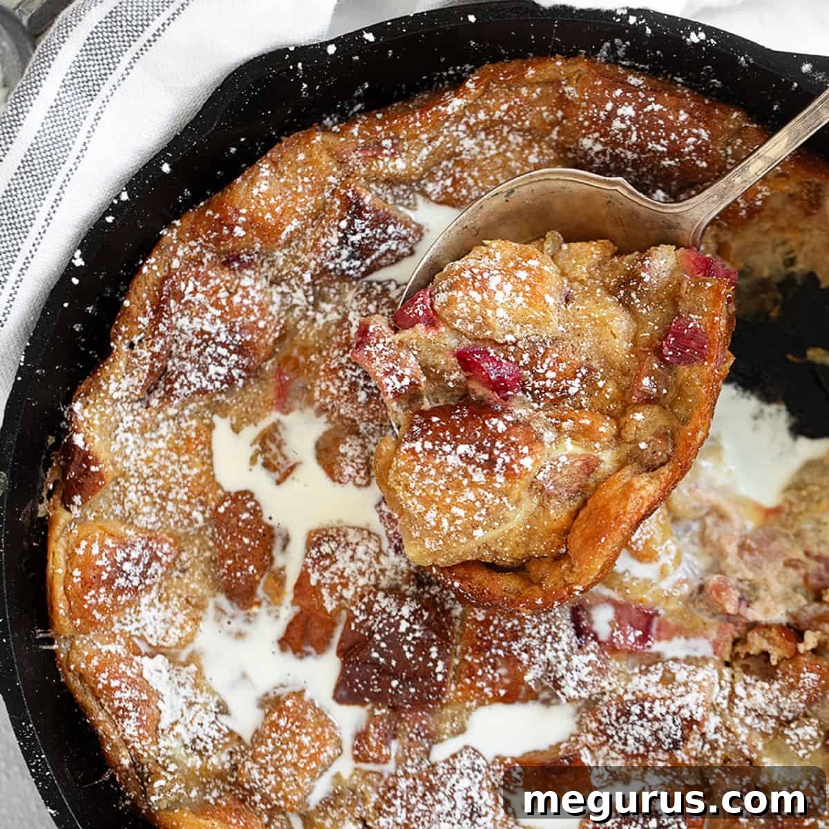 Rhubarb bread pudding served in a cast iron skillet with a spoon.
