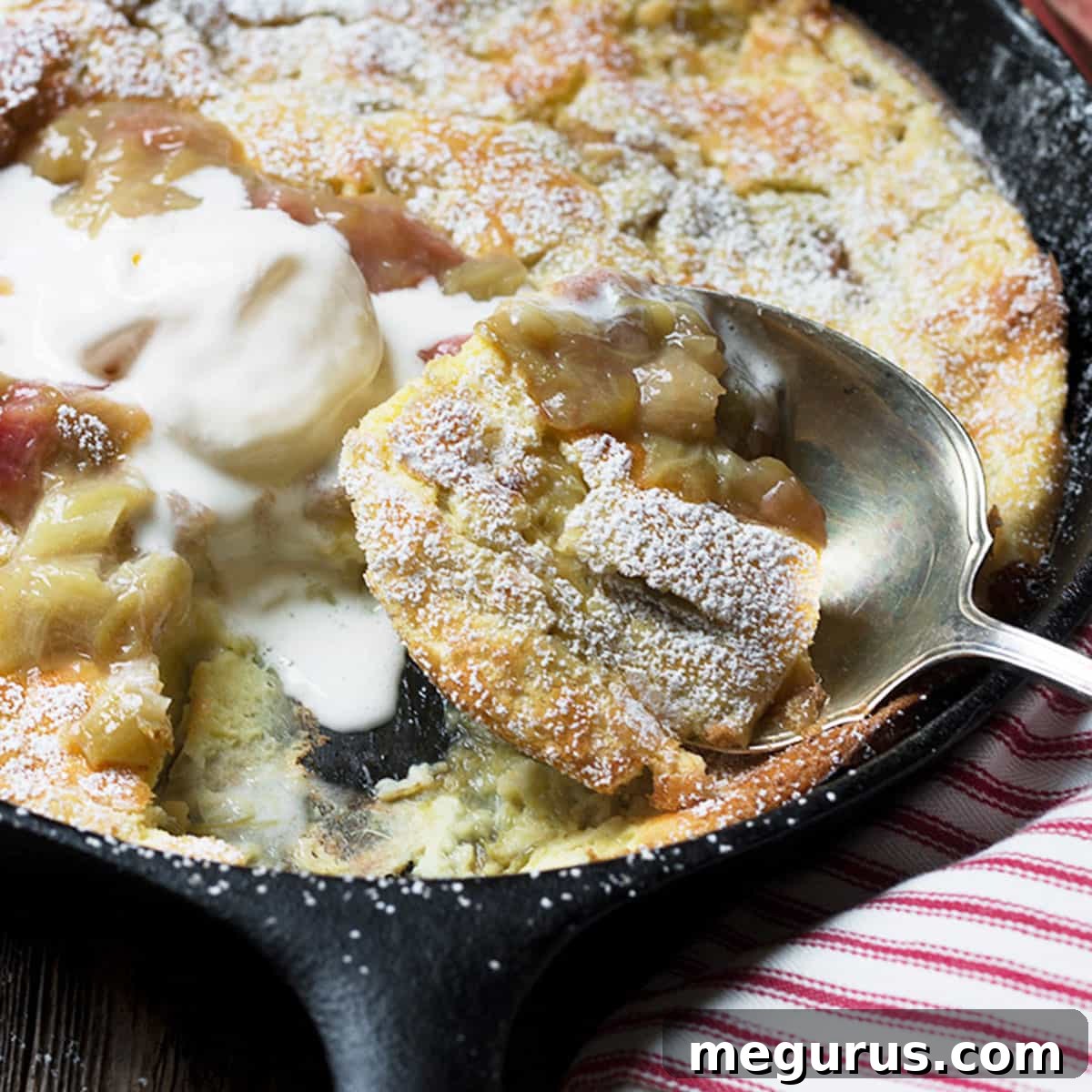 A Rhubarb Dutch Baby in a cast iron skillet, dusted with powdered sugar.
