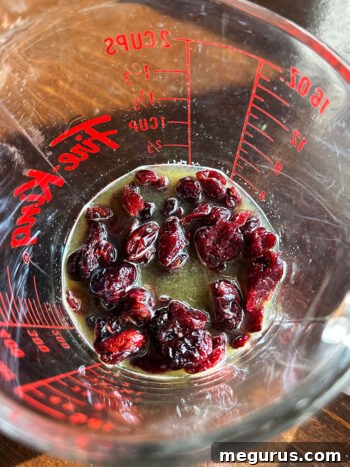 Dried cranberries soaking in warm orange juice, becoming plump and flavorful.