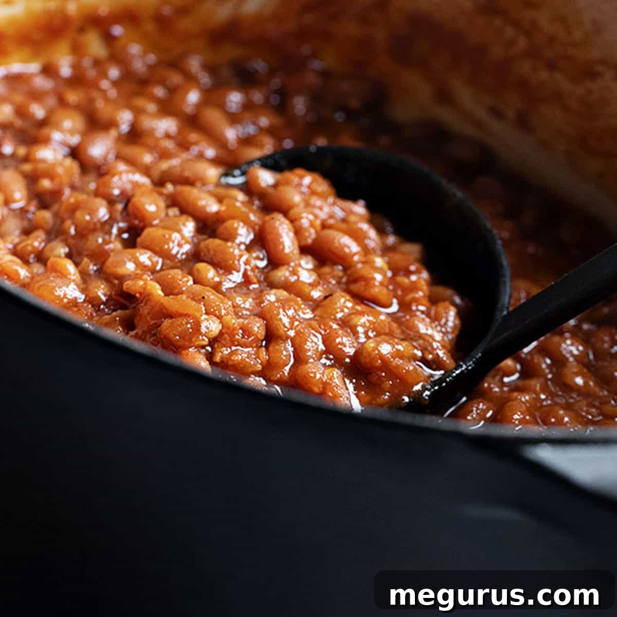 homemade baked beans in black casserole with ladle
