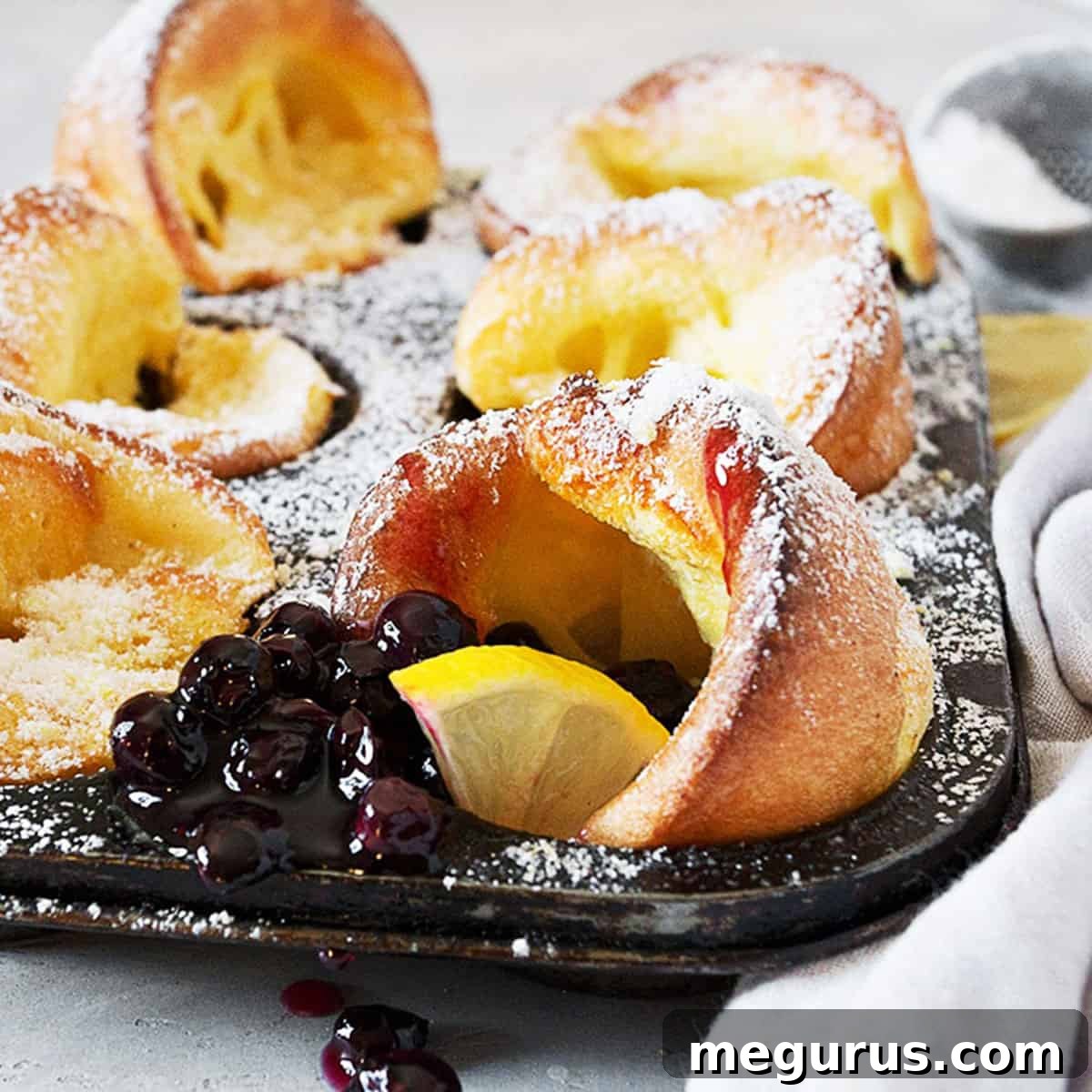 mini Dutch babies in muffin tin with lemons and blueberry sauce