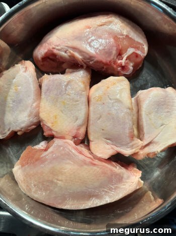 Raw bone-in, skin-on chicken pieces seasoned in a baking pan.