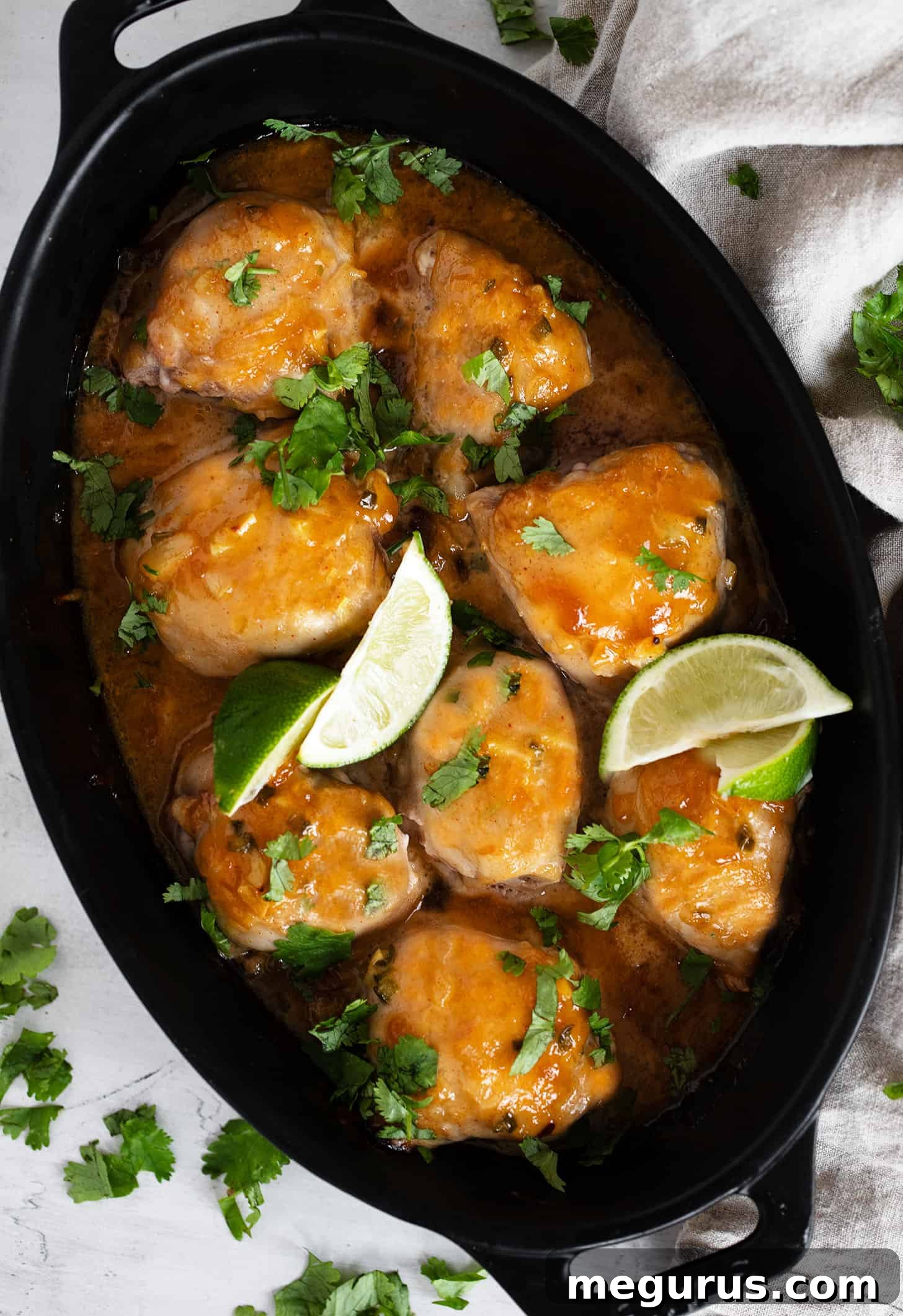 Close-up of baked mango chutney chicken in a baking dish, garnished with fresh herbs