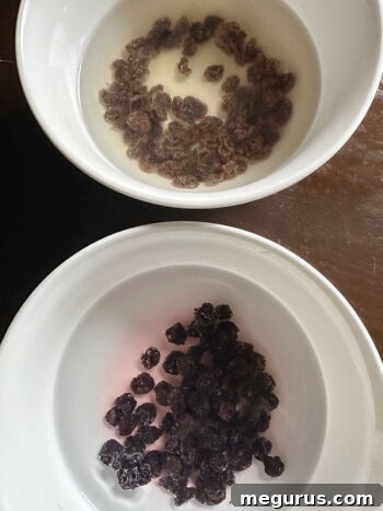 Dried blueberries and raisins plumping in hot water in separate bowls, ready for the dough.