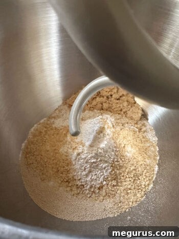 Dry ingredients being added to the bowl of a stand mixer, preparing for dough mixing.