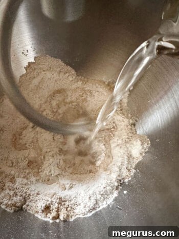 Lukewarm water being poured into the dry ingredients in the mixer bowl to form the dough.