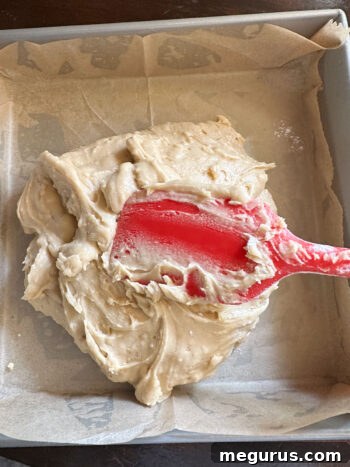 Spooning blondie batter into a prepared 9x9 inch baking pan