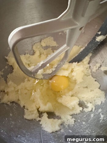 Adding an egg to the creamed butter and sugar mixture, showing the smooth, pale yellow batter.