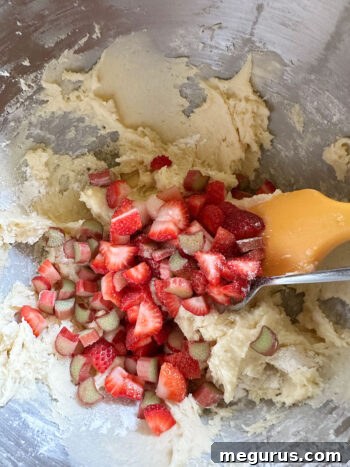 Adding freshly chopped strawberries and rhubarb pieces to the muffin batter.