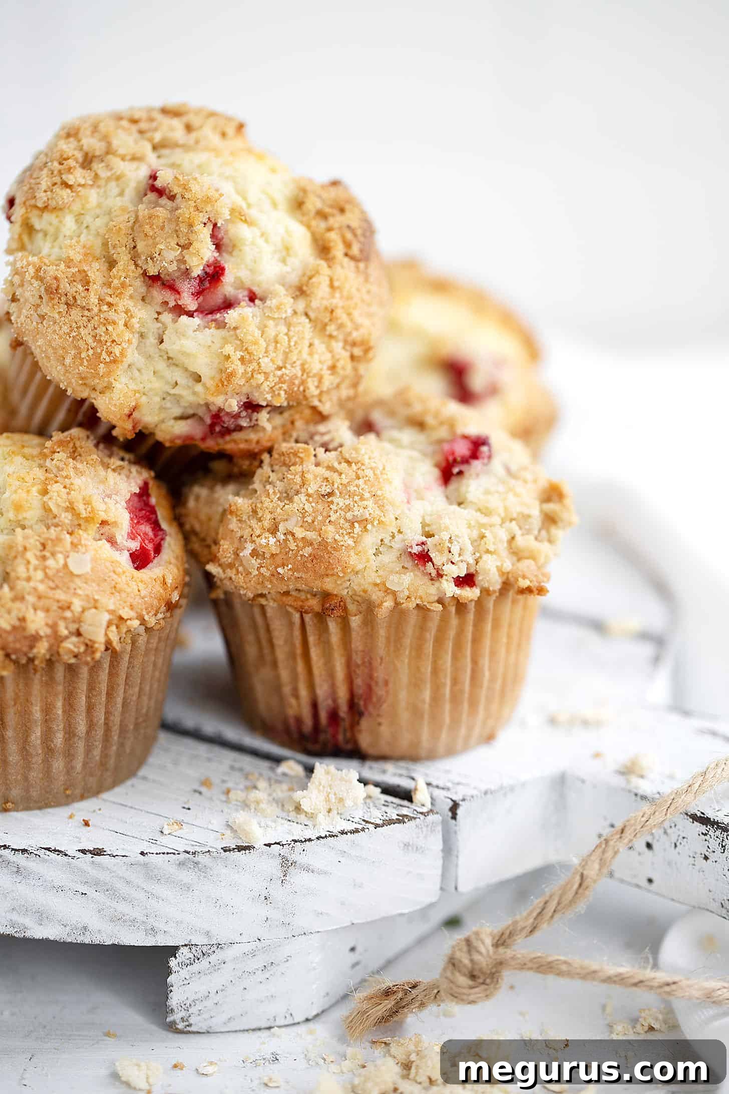 A close-up shot of baked strawberry rhubarb muffins with streusel, presented beautifully on a wooden serving board.