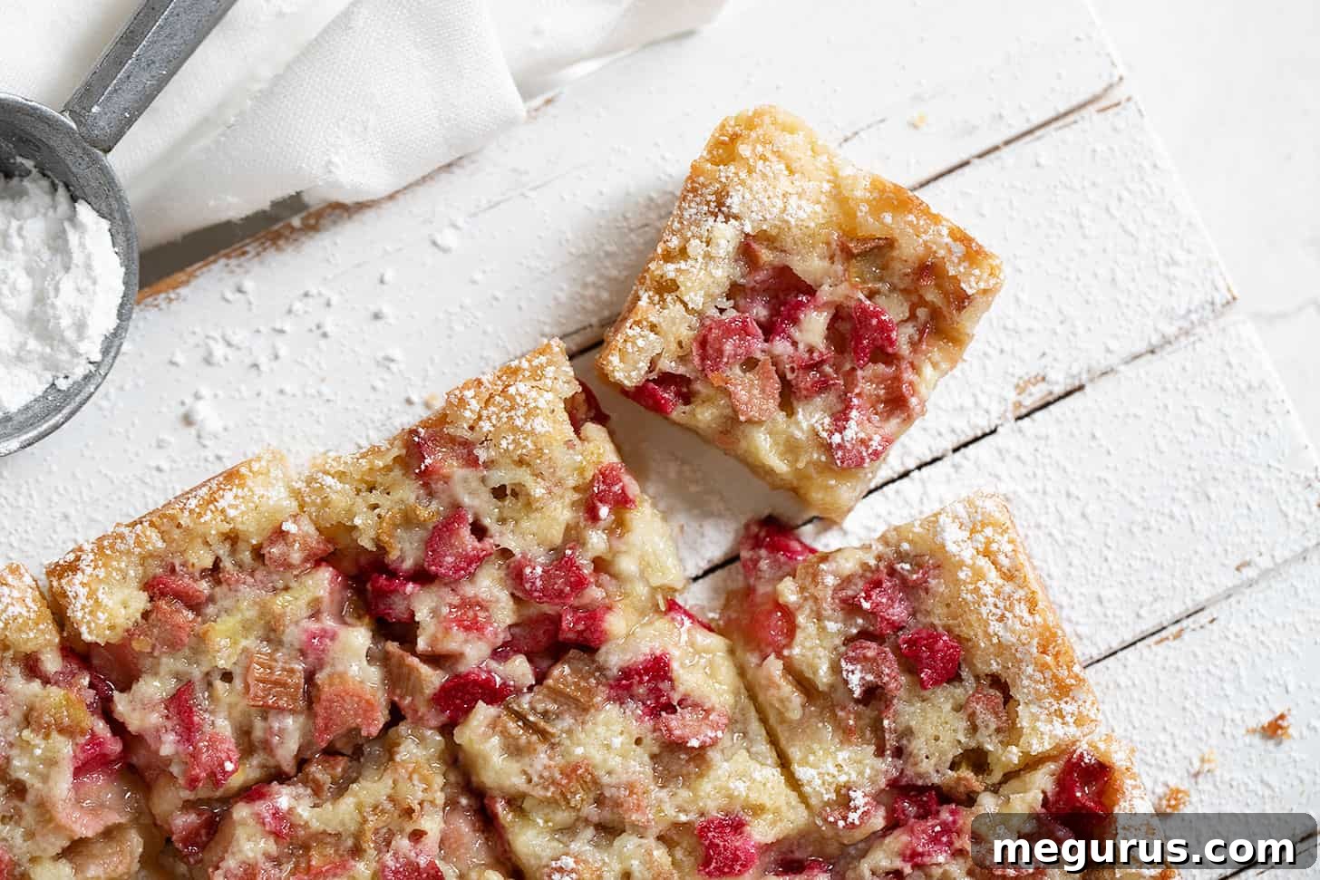 Freshly baked rhubarb bars cut into squares on a wooden serving board, showcasing the layers of shortbread crust and pink custard topping.