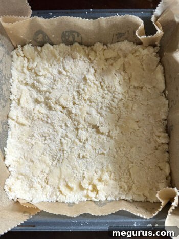 Shortbread base pressed evenly into a parchment-lined 8x8 inch baking pan.