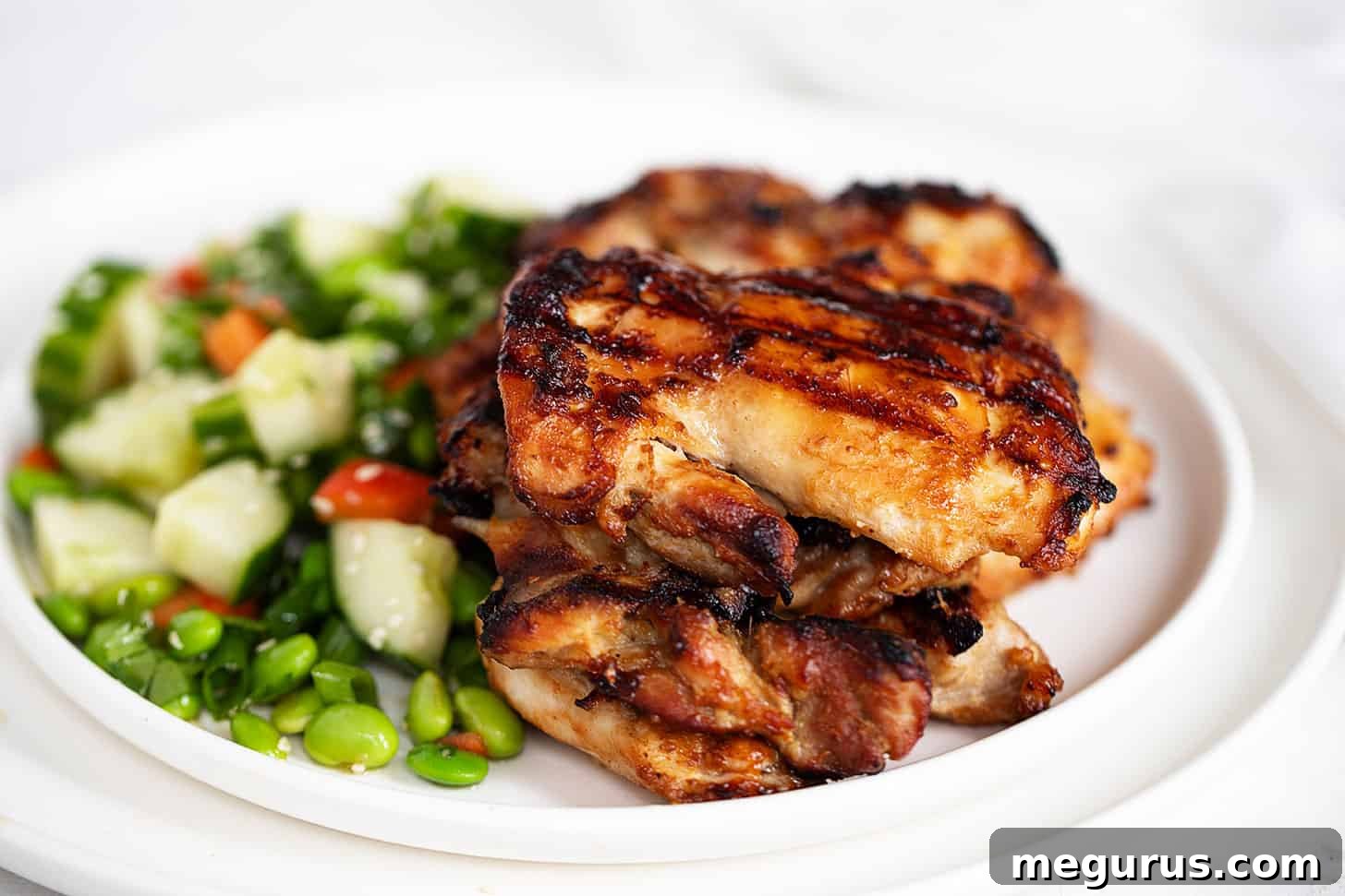 Perfectly grilled miso chicken thighs on a plate, served alongside a vibrant edamame salad.