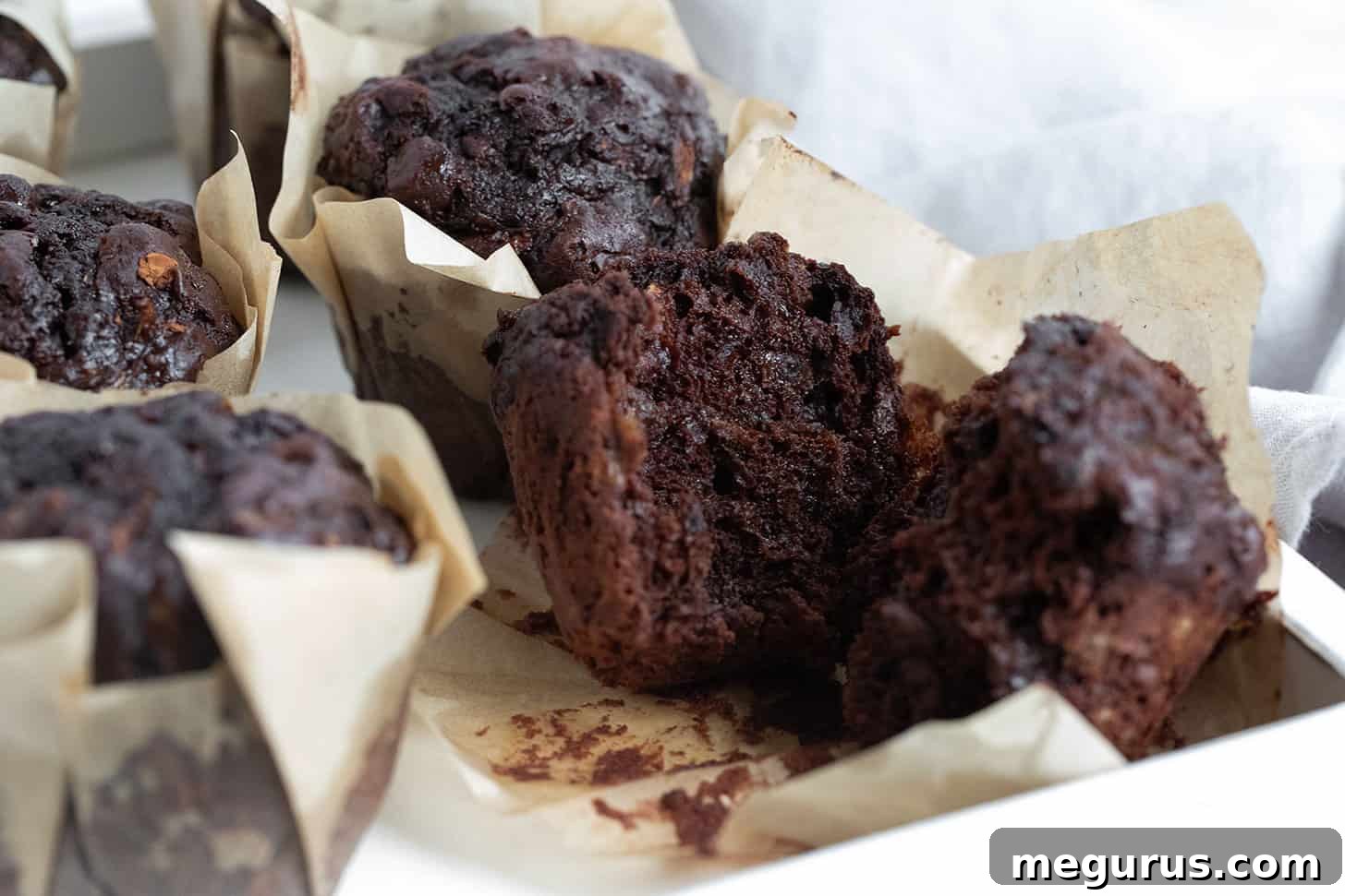 Rich double chocolate zucchini muffins split open, revealing their moist interior and walnuts.