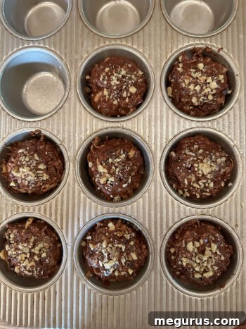 Muffin batter scooped into baking cups, topped with extra walnuts before baking.