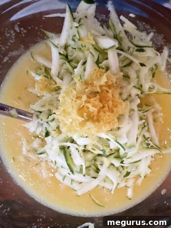 Wet ingredients including eggs, oil, vanilla, sugar, lemon zest, and shredded zucchini being mixed together in a bowl.