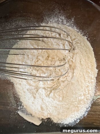 Dry ingredients including flour, baking powder, salt, and baking soda being whisked together in a separate bowl.