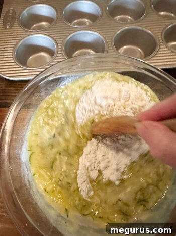 A spatula gently stirring the muffin batter, showing it is just barely combined with some flour streaks visible.