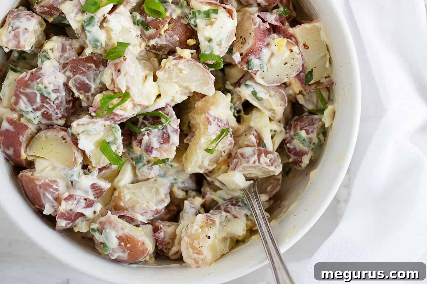 Creamy potato egg salad in a white bowl with a spoon, ready to be served