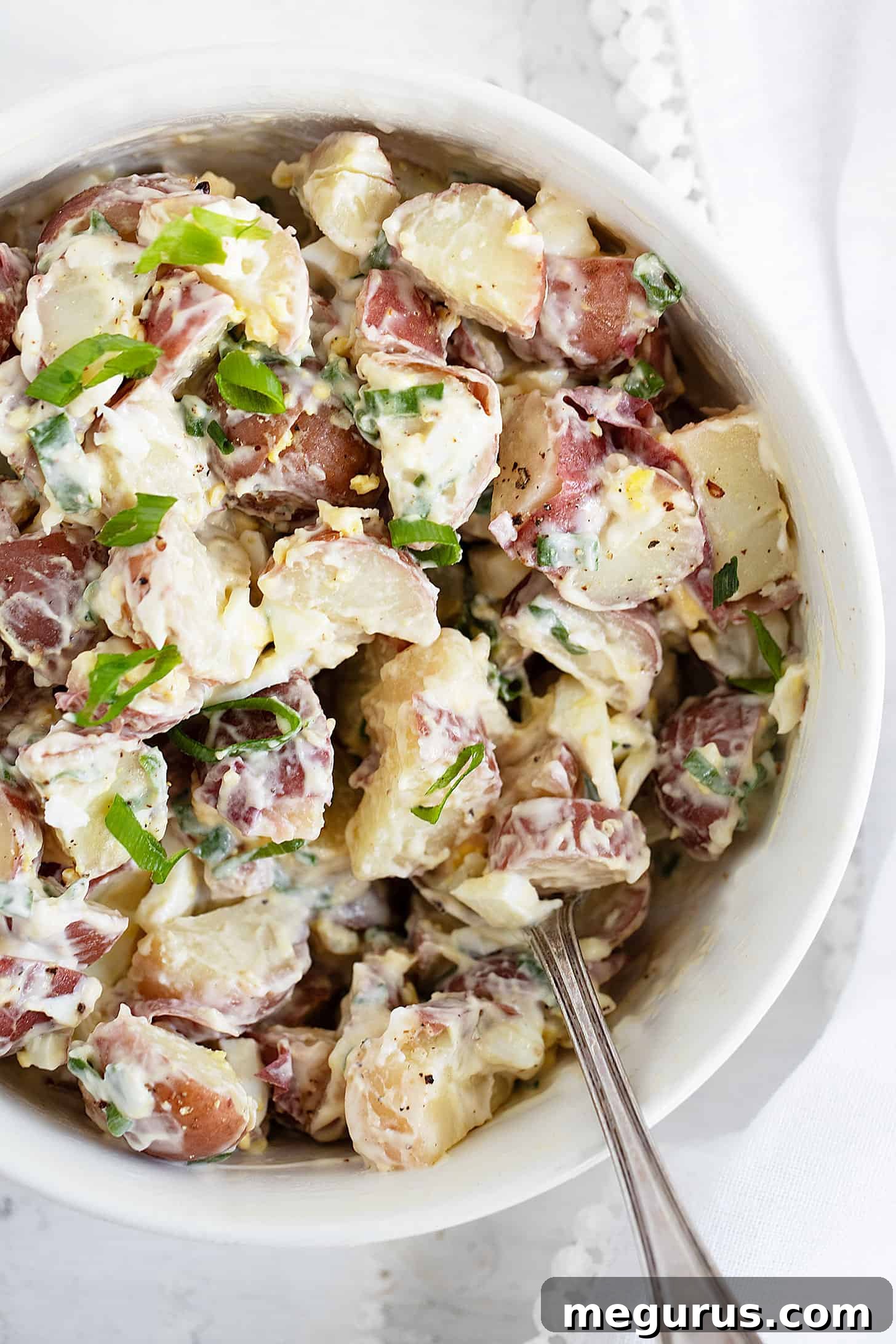 Close-up of potato egg salad in a white bowl with a serving spoon