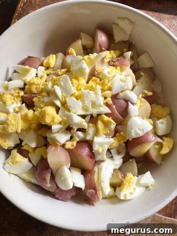 Adding chopped hard-boiled egg to potatoes in a mixing bowl