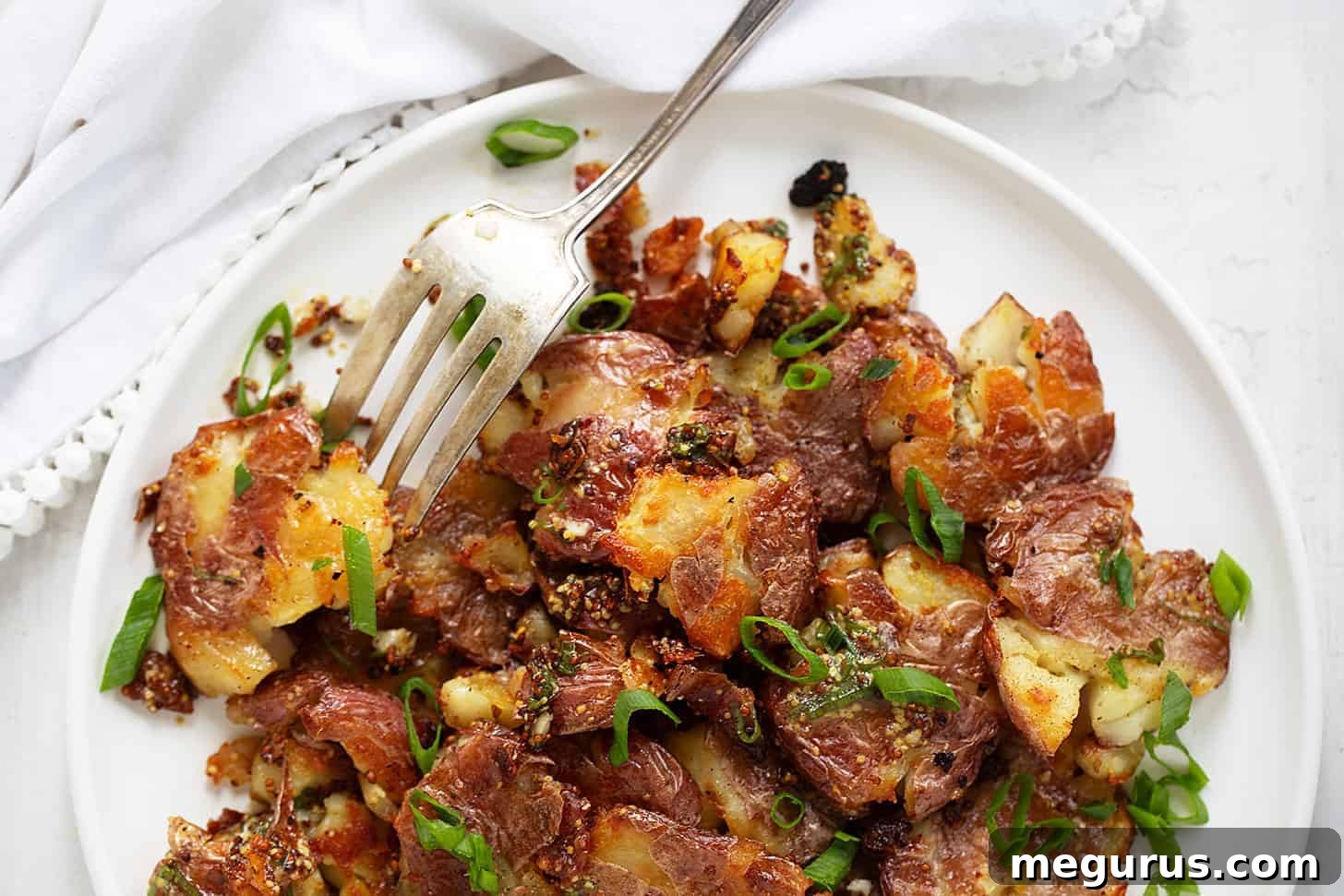 A plate of warm smashed potato salad with a fork, showing crispy potato edges and vibrant green herbs.