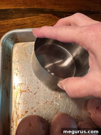Smashing boiled potatoes with the bottom of a measuring cup on a baking sheet.