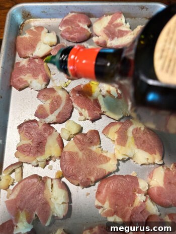 Drizzling olive oil over smashed potatoes on a baking sheet before roasting.